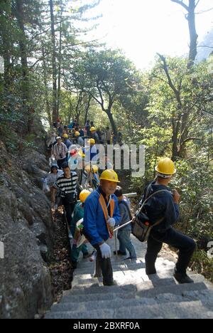 Huangshan Mountain dans la province d'Anhui, Chine. Ouvriers grimpant les marches est de Huangshan transportant un très long tuyau. Banque D'Images