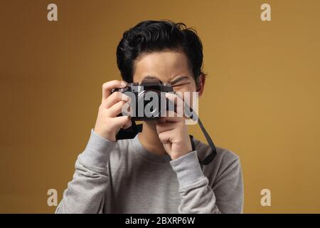 Joyeux garçon asiatique faisant des activités de loisirs de photographie, enfant comme photographe prenant des photos avec son appareil photo numérique, sur fond jaune Banque D'Images