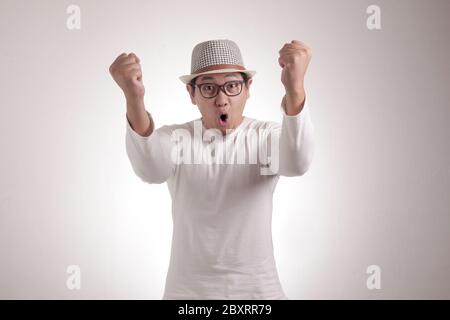 Le portrait d'un jeune homme d'affaires asiatique prospère montre un geste gagnant, célébrant la victoire. Mains soulevées au-dessus Banque D'Images