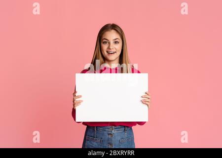 Bonne fille adolescente souriante tenant une feuille blanche de papier dans les mains avec un espace vide Banque D'Images