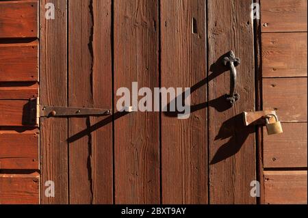 Porte en bois peint marron verrouillée par cadenas et longues ombres Banque D'Images