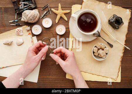 La femme tient une vieille clé dans ses mains. Sur la table sont des feuilles de papier vierges, des vieilles lettres et une tasse de thé. Souvenir du passé lointain. Banque D'Images