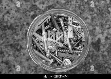 Photo en noir et blanc de boulons et écrous assortis dans un bol en verre avec fond de pierre à grinder et espace de copie flou. Rangement de matériel métallique dans l'op Banque D'Images