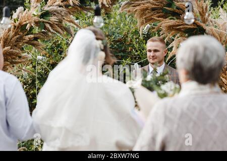 Marié debout près de l'arche de mariage et regardant la mariée qui le mène à lui. Mariée et marié. Cérémonie de mariage Banque D'Images