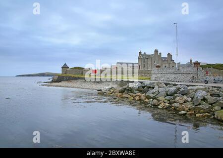 Côte avec galets et rochers et jetée de Sandsayre par une journée d'été grise, Sandwick, îles Shetland, Écosse. Banque D'Images