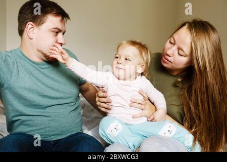 Jeunes parents de 30s tenant sur les mains naughty petite fille enfant avec l'expression drôle sur son visage Banque D'Images