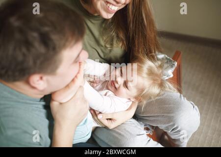 Bonne famille dans des vêtements décontractés à la maison, les jeunes parents jouant avec leur tout-petit drôle joyeuse fille Banque D'Images