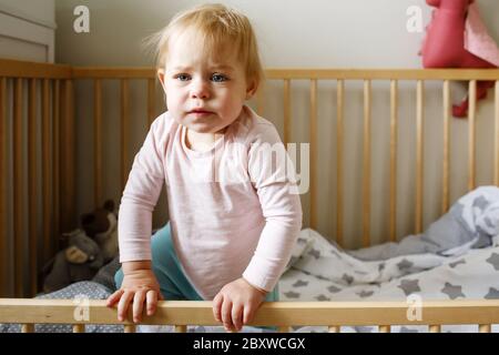 Une petite fille bouleversée se tenant dans un lit de bébé, berceau essayant de sortir Banque D'Images