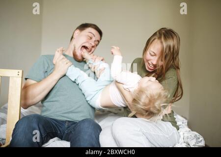 Bonne famille dans des vêtements décontractés à la maison, les jeunes parents jouant avec leur tout-petit drôle joyeuse fille Banque D'Images