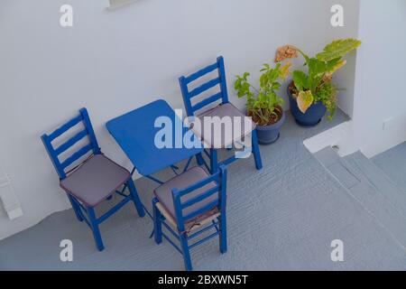 Août à l'île de Serifos, Grèce. Une petite table bleu fer, avec trois chaises en bois bleu ancien. Deux pots bleus avec des fleurs à côté de la table . Banque D'Images