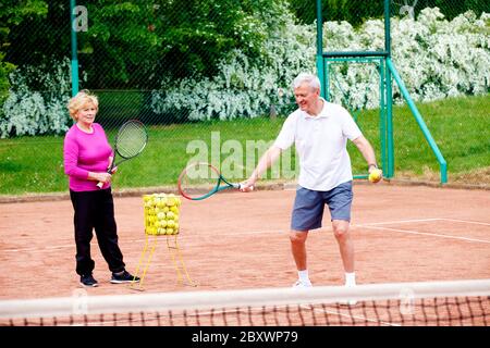 Photo en plein air d'un homme âgé enseignant une femme âgée jouant au tennis sur le court de tennis. Banque D'Images