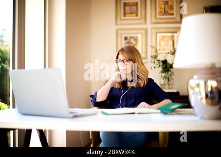 Photo d'une femme d'affaires d'âge moyen utilisant un écouteur, assise derrière son ordinateur portable et ayant des discussions et des réunions en ligne en vidéoconférence. Femme d'affaires Banque D'Images