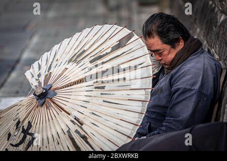 Un vendeur japonais de parasols en papier prenant une sieste dans la rue Ninenzaka, qui mène au sanctuaire Kiyomizu-dera à Kyoto, Japon Banque D'Images