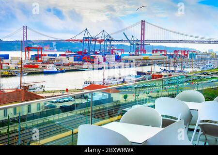 Vue sur le port commercial de Lisbonne depuis la terrasse extérieure du restaurant, les conteneurs, les grues de fret, les bateaux à moteur, les voies ferrées et le parking, pont du 25 avril Banque D'Images