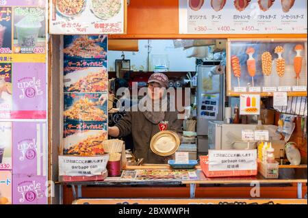 Jeune femme vendeur dans sa cuisine de restauration rapide de son stalle / restaurant à Ameyoko Market, Tokyo, Japon Banque D'Images