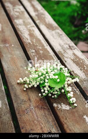 Bouquet de lys frais de la vallée sur une surface en bois, gros plan. Petites fleurs blanches parfumées dans un bouquet romantique. Banque D'Images