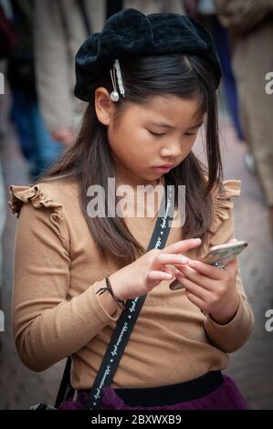 Une jeune fille marchant et utilisant son smartphone dans la rue Takeshita, Harajuku, Tokyo, Japon Banque D'Images