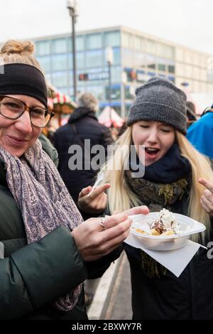 Deux femmes touristes partagent un dessert sucré et délicieux provenant d'une cabine de cuisine extérieure au marché de Noël Alexanderplatz, Mitte, Berlin Banque D'Images