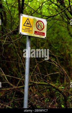 Ces panneaux d'avertissement sont sur un chemin menant à travers un bois à l'étang de pêche local. Ils avertissent des lignes électriques aériennes. Banque D'Images