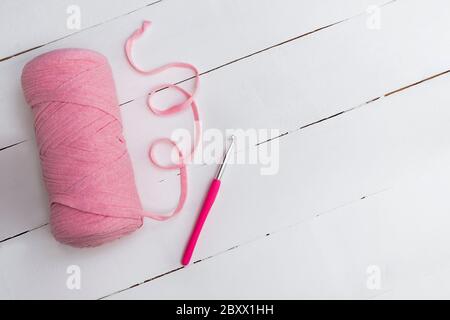 Vue de dessus du fil de ruban rose avec crochet crochet sur table en bois blanc avec espace pour le texte. Expérience artisanale et de bricolage Banque D'Images