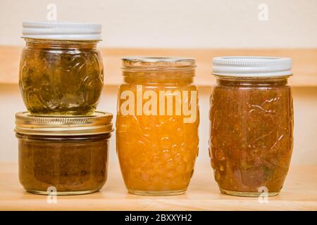 Articles en conserve maison sur une étagère à manger, de gauche à droite : gelée de poivre sur le beurre de poire, confiture de pêche et salsa Banque D'Images