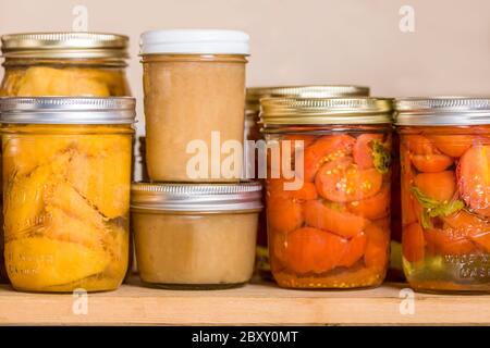 Étagère à pantry de conserves, de gauche à droite : pêches de paradis rouge, compote de pommes biologique et tomates de juilette biologiques Banque D'Images