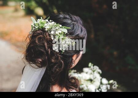 Gros plan de la coiffure de la mariée de brunette. Vue arrière de la coiffure de mariage avec fleurs blanches / vertes fraîches. Concept de mariage. Banque D'Images