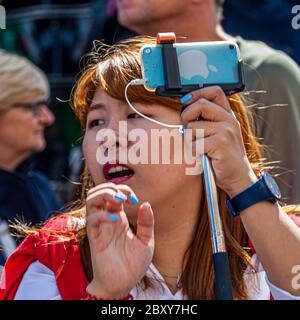 Une jeune femme s'occupe d'un bâton de selfie dans l'agitation de la rue. Royal Borough de Kensington et Chelsea, Angleterre Banque D'Images