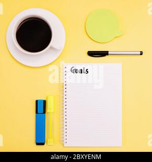 Objectifs Flat Lay photo texte d'action sur carnet, accessoires de bureau et tasse de café noir sur fond jaune Banque D'Images