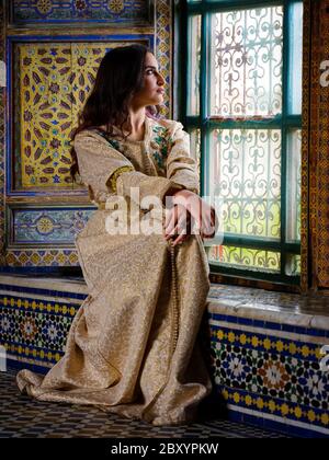 FÈS, MAROC - VERS MAI 2018 : jeune femme marocaine en robe traditionnelle assise par une fenêtre à Fès Banque D'Images