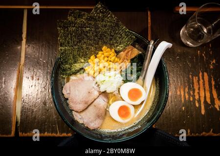 Un bol de nouilles ramen avec du porc, des œufs et des feuilles de nori sur un comptoir en bois typique dans un restaurant traditionnel de Tokyo Banque D'Images