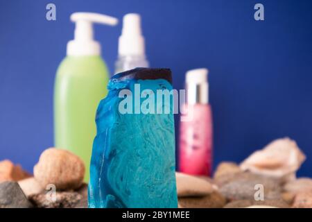 Fine pièce plate de savon à la main de menthe bleue posée sur des cailloux et des articles de toilette derrière Banque D'Images