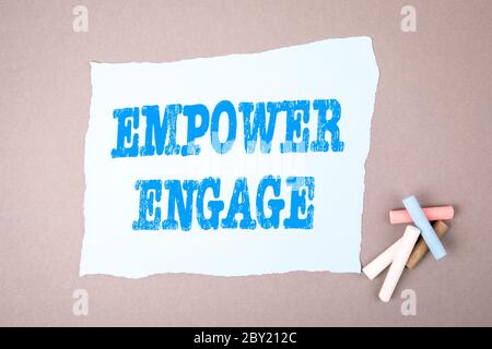 CONCEPT EMPOWER ENGAGE. Texte sur la feuille de notes. Crayons de couleur sur une table grise Banque D'Images