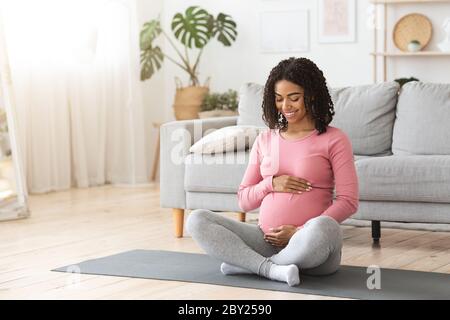 Une femme enceinte heureuse qui épouse son ventre à la maison Banque D'Images