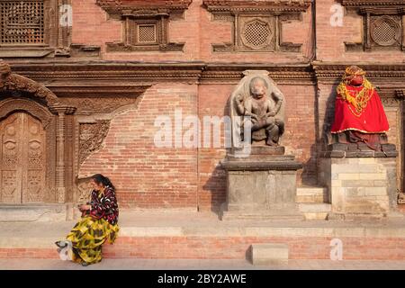 Une femme se trouve devant le palais royal, la place Durbar, Patan (Lalitpur), au Népal, près d'une statue Hanuman vêtue de rouge (r) et d'une frise de Bhairav (Shiva) Banque D'Images