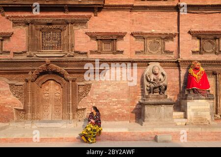 Une femme se trouve devant le palais royal, la place Durbar, Patan (Lalitpur), au Népal, près d'une statue Hanuman vêtue de rouge (r) et d'une frise de Bhairav (Shiva) Banque D'Images