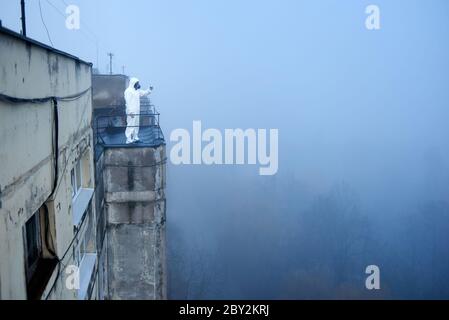 Instantané d'un grand toit plat d'un bloc d'appartements en ville, journée brumeuse et un scientifique menant ses recherches sur la pollution de l'air, copier l'espace. Homme en vêtements de protection et masque à gaz Banque D'Images