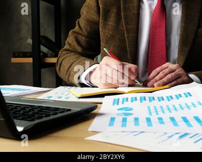 Homme d'affaires prend des notes dans un ordinateur portable tout en étant assis sur un lieu de travail au bureau. Banque D'Images