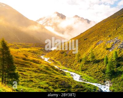 Matin dans la vallée alpine avec brume éclairée par le soleil levant, les prairies verdoyantes et la petite rivière, Autriche. Banque D'Images