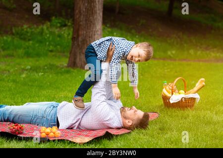 Passe-temps en famille à l'extérieur. Jeune père jouant avec son petit fils drôle pendant le pique-nique à l'extérieur, espace libre Banque D'Images