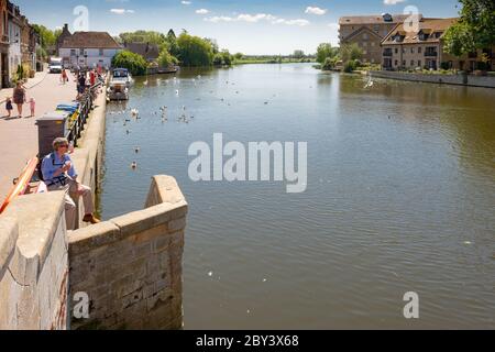 Vue panoramique sur une rivière idyllique de l'est de l'Anglia. Le mur de pierre montre un homme qui profite du soleil avec des gens à distance nourrissant des canards locaux. Banque D'Images