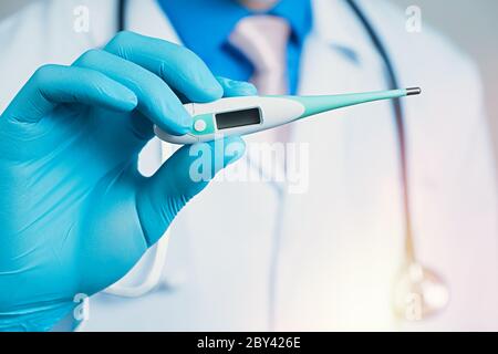 Vue rapprochée du thermomètre avec gant bleu en caoutchouc portant la main, poitrine de l'homme avec peignoir médical blanc sur fond flou avec stéthoscope Banque D'Images