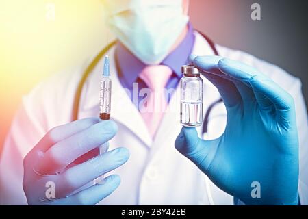 Vue rapprochée de la seringue et de l'ampoule en verre avec les mains vêtues de gants en caoutchouc bleu, robe blanche habillée médecin sur fond flou Banque D'Images