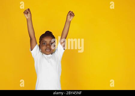 Fort, gagnant, leader. Portrait de petite fille afro-américaine sur fond jaune studio. Joyeux, beau enfant. Concept des émotions humaines, expression, ventes, publicité. CopySpace. Il est mignon. Banque D'Images