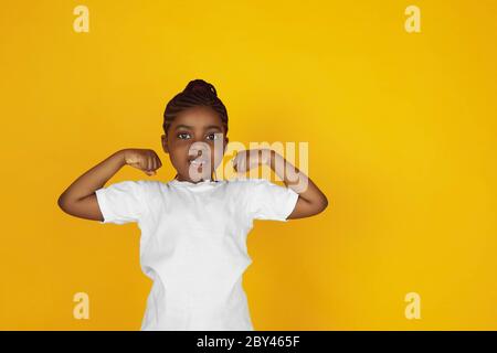 Fort, gagnant, leader. Portrait de petite fille afro-américaine sur fond jaune studio. Joyeux, beau enfant. Concept des émotions humaines, expression, ventes, publicité. CopySpace. Il est mignon. Banque D'Images