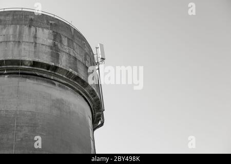 Tour d'eau en béton coulé très abîmé, vu contre un ciel bleu clair. Les mâts de télécommunication 5G récemment installés sont visibles au sommet de la tour. Banque D'Images