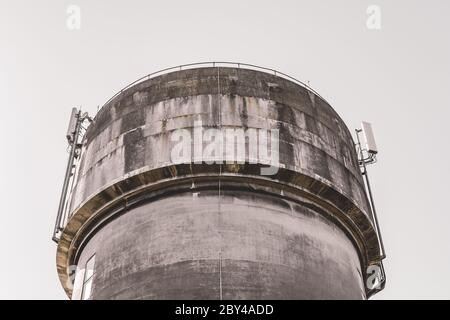 Tour d'eau en béton coulé très abîmé, vu contre un ciel bleu clair. Les mâts de télécommunication 5G récemment installés sont visibles au sommet de la tour. Banque D'Images