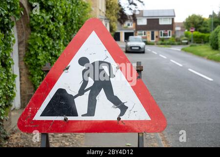 Gros plan d'un panneau de travaux routiers typique situé sur une zone de chaussée. Une voiture garée éloignée est vue, les grands travaux routiers sont à proximité, ce qui cause des problèmes de circulation. Banque D'Images