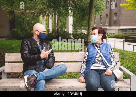 La vieille femme avec son fils mature portant un masque facial assis sur un banc extérieur en gardant la distance sociale dans la nouvelle normale Banque D'Images