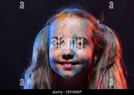 Fille avec visage souriant sur fond noir, gros plan. Une écolière a des taches de peinture sur le visage. Enfant avec des queues de cheval fait art. Concept d'enfance et de vacances. Banque D'Images